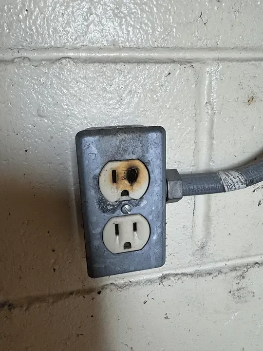 A scorched duplex receptacle in a metal box on a block wall, found during a repair call