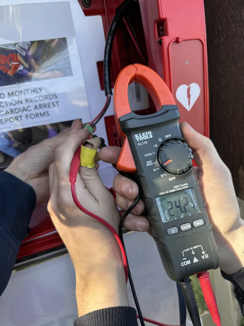 Hands holding a clamp meter reading a circuit while troubleshooting