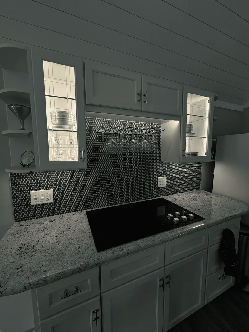A kitchen with under-cabinet lighting along a tile backsplash and lit glass-front cabinets
